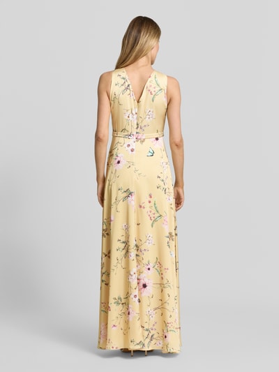 Modelka nosi sukienka wieczorowa 'Abendkleid mit rückseitigem V-Ausschnitt' od V.M. z satyny, linia a, długa sukienka, marszczenia, dekolt na plecach, zamek błyskawiczny z tyłu, długość tyłu w rozmiarze 36: 133 cm, szerokość w rozmiarze 36: 35 cm, pastelowy żółty z kwiatowym wzorem, widok całej sylwetki z tyłu.