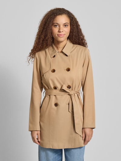 Modelka kobieca nosi Regular Fit Trenchcoat mit doppelreihiger Knopfleiste Modell 'VALERIE' od Only, jednolity, pasek w talii, długi rękaw, kieszenie boczne, krój regular fit, beżowy, widok całej sylwetki z przodu.