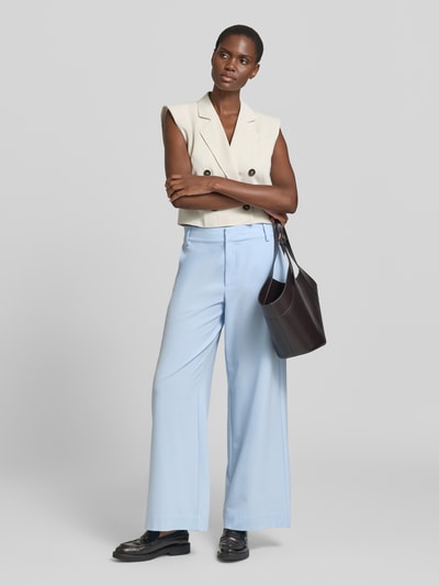 Modelka nosi spodnie z szerokimi nogawkami Wide Leg Hose mit Viskose-Anteil Modell 'Hace' od My Essential Wardrobe, mieszanka materiałów z dodatkiem wiskozy, wpuszczane kieszenie, zapięcie na haftkę i zamek błyskawiczny, szerokość w rozmiarze 36: 40 cm, długość wewnętrzna nogawki w rozmiarze 36: 79 cm, jasnoniebieski kolor, gładka faktura, widok całej sylwetki z przodu.