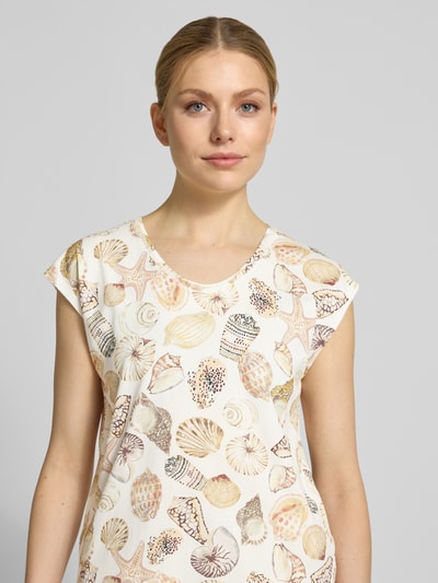 Modelka kobieca nosi Regular Fit T-Shirt mit Allover-Motiv-Print od Marc Cain, bawełniana mieszanka, jasne kolory, okrągły dekolt, długość tyłu 58 cm w rozmiarze 36, krój regular fit, zbliżenie na górną część ciała.