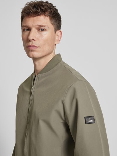 Männermodel trägt olivgrüne Bomberjacke mit Stehkragen Modell 'BLAASPEN' von Jack & Jones Premium, Material-Mix, Nahaufnahme Oberkörper.