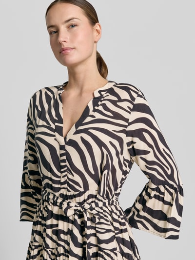 Vrouwenmodel draagt Tailliertes Tunikakleid aus reiner Viskose Modell 'MELBA' van Vero Moda met all-over print, v-hals, trompetmouwen, volantzoom en bindriem, mini lengte, getailleerde fit, detailopname bovenlichaam.