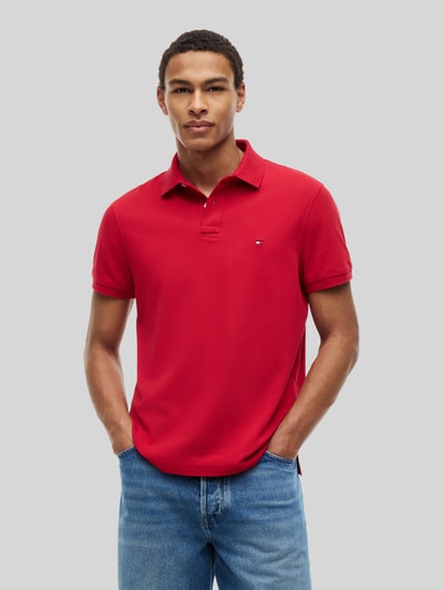 Männermodel trägt rotes Regular Fit Poloshirt aus Baumwoll-Mix von Tommy Hilfiger, kombiniert mit blauer Jeans, Ganzkörperansicht von vorne.