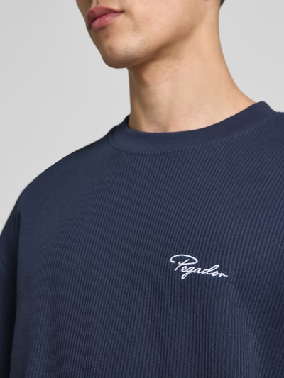 Männermodel trägt Oversized T-Shirt mit Strukturmuster von Pegador, Baumwoll-Mix, Logo-Stitching, Rundhalsausschnitt, Nahaufnahme Oberkörper.