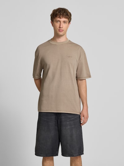 Męski model nosi Oversized T-Shirt mit Label-Stitching od Pegador z czystej bawełny, kolor beżowy, okrągły dekolt, Ganzkörperansicht von vorne. Długość pleców w rozmiarze M: 70 cm.