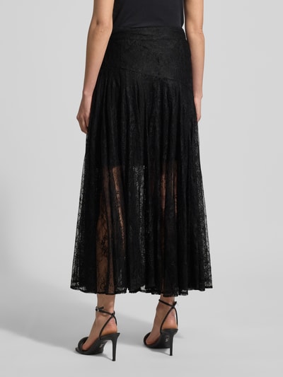 Vrouwenmodel draagt zwarte Spitzenrock in A-Linie Modell 'LEA' van Copenhagen Muse, transparante kantstructuur, maxi lengte, bandwijdte maat S 37 cm, totale lengte 95 cm. Volledige lichaamsaanzicht achteraan.