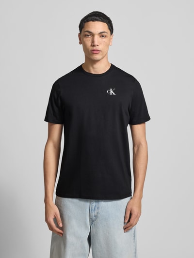 Männermodel trägt Regular Fit T-Shirt mit Logo-Print von Calvin Klein Jeans in Schwarz, reine Baumwolle, Rundhalsausschnitt, Ganzkörperansicht von vorne.