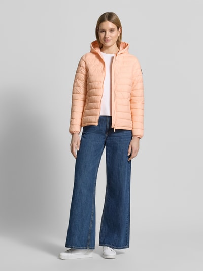 Frauenmodel trägt Steppjacke mit Kapuze Modell 'THELMA' von CARS JEANS in zartem Apricot, Regular-Fit, Reißverschluss, Eingrifftaschen, dazu blaue Jeans und weiße Schuhe, Rückenlänge 61 cm, Schulterbreite 39 cm, Brustweite 50 cm, Ärmellänge 62 cm, Ganzkörperansicht von vorne.
