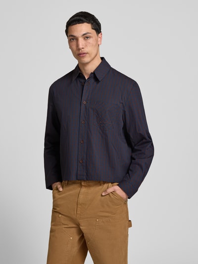 Mannelijk model draagt Relaxed Fit vrijetijdsoverhemd met borstzak van KARL KANI, donkerblauw met bruine strepen, puur katoen, borstzak, gestikt logo, met lange mouwen, kentkraag en knoopsluiting, ruglengte maat M 65 cm, schouderbreedte maat M 49 cm, mouwlengte maat M 66 cm, detailopname van voren.