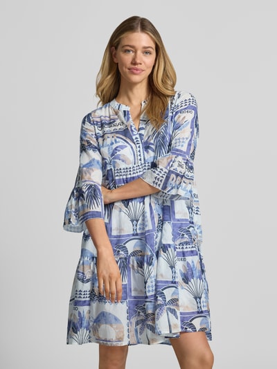 Frauenmodel trägt Tunikakleid im Allover-Look mit V-Ausschnitt von Emily Van den Bergh, Reine Baumwolle, A-Linie, Minikleid, Trompetenärmel, blau-weißes Muster, weiche Textur, Ganzkörperansicht von vorne.