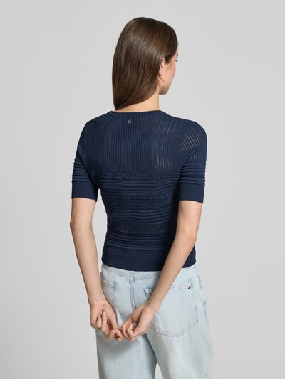 Frauenmodel trägt T-Shirt in Strick-Optik mit Rundhalsausschnitt von Guess im Material-Mix mit Viskose-Anteil, Körpernaher-Schnitt, Rückansicht.