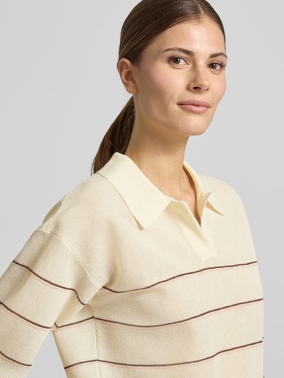 Modelka kobieca nosi Strickshirt aus Viskose-Mix mit Polokragen Modell 'Pringi' od OPUS, kremowy w paski, krój regular fit, z dekoltem w serek, długość tyłu w rozmiarze 36: 52 cm, długość rękawa w rozmiarze 36: 24 cm, półzbliżenie górnej części ciała.
