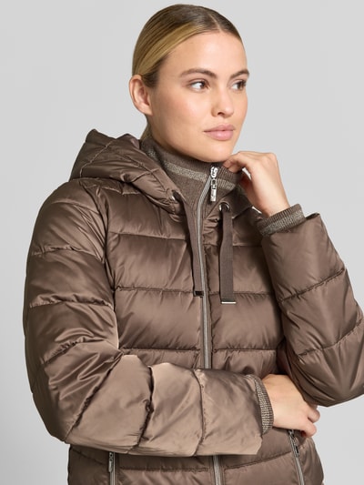 Vrouwenmodel draagt Regular Fit lange jas in stiksels van monari, capuchon met tunnelkoord, opstaande kraag, steekzakken met ritssluiting, tweewegritssluiting, detailopname bovenlichaam