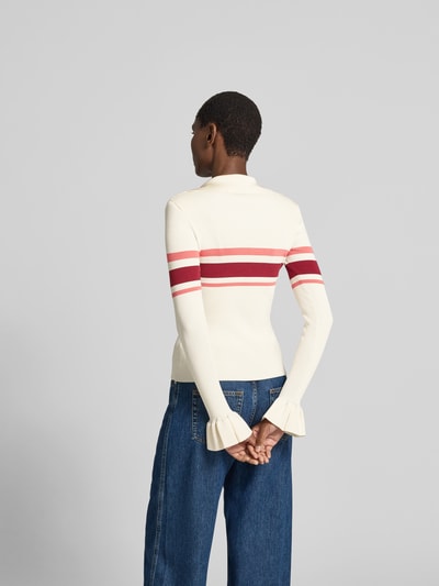 Frauenmodel trägt Strickjacke aus Viskose-Mix von Self-Portrait in Creme mit roten Streifen, eng anliegende Passform, Umlegekragen, geraffte Ärmelabschlüsse, Knopfleiste, Rückenlänge 55 cm, Brustweite 38 cm, Ärmellänge 68 cm, Ganzkörperansicht Rückansicht.