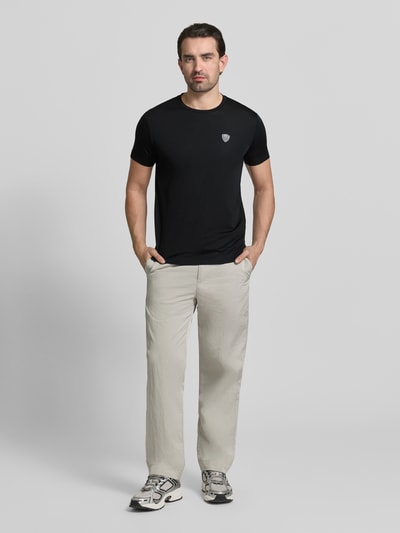 Mężczyzna nosi T-Shirt aus Viskose-Mix mit Label-Patch von EA7 Emporio Armani, czarny kolor, krój slim fit, okrągły dekolt, materiał z rozciągliwym dodatkiem, długość tyłu w rozmiarze M: 69 cm, Ganzkörperansicht von vorne.