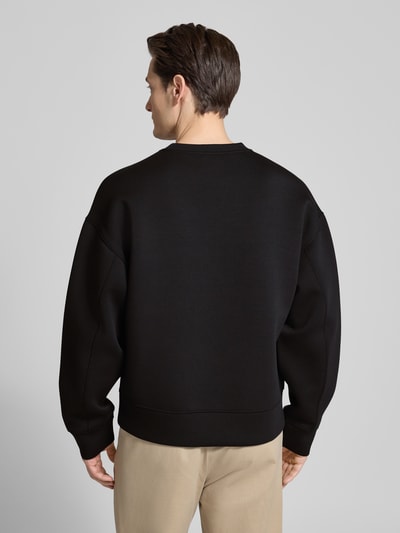 Männermodel trägt czarną bluzę 'Sweatshirt mit Rundhalsausschnitt und Logo' von CK Calvin Klein, mieszanka materiałów z dodatkiem wiskozy, krój regular fit, okrągły dekolt, długość tyłu w rozmiarze M: 61 cm, długość rękawów w rozmiarze M: 59 cm, widok całej sylwetki z tyłu.