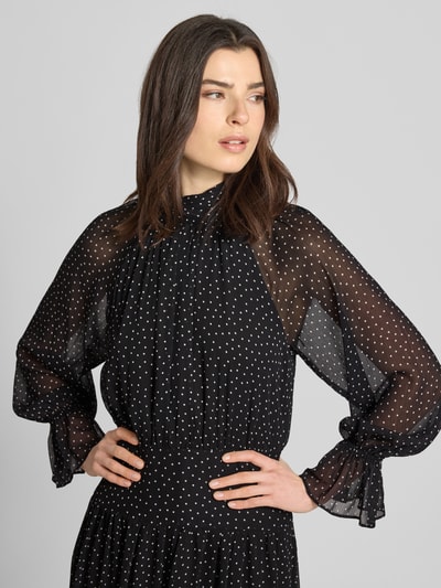 Frauenmodel trägt Damen Midikleid mit kleinem Stehkragen Modell 'POLKY' von Mango aus schwarzem Chiffon mit weißen Punkten, taillierter Schnitt, Raglanärmel, elastische Ärmelabschlüsse, Rückseitiger Reißverschluss, Rückenlänge 126 cm, Brustweite 38 cm, Ärmellänge 56 cm, Nahaufnahme Oberkörper.