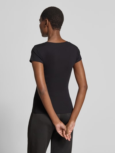 Frauenmodel trägt Slim Fit T-Shirt mit Logo-Applikation von Guess aus elastischem Baumwoll-Mix in Schwarz, Ganzkörperansicht Rückansicht.