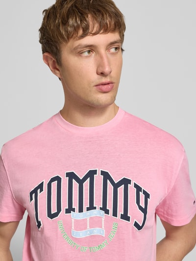 Männermodel trägt Regular Fit T-Shirt aus reiner Baumwolle von Tommy Jeans in Rosa mit Logo-Print, Nahaufnahme Oberkörper. Herren T-Shirt von Tommy Jeans.