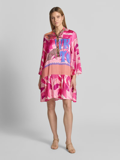 Frauenmodel trägt Relaxed Fit Minikleid aus reiner Viskose mit Animal-Print von miss goodlife in Pinktönen mit Knopfleiste, Stehkragen, langärmeligem Design, Ganzkörperansicht von vorne. Rückenlänge bei Größe S: 100 cm, Brustweite: 37 cm, Ärmellänge: 58 cm.