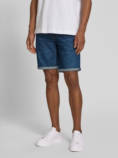 Männermodel trägt Slim Fit Jeansshorts aus Baumwoll-Mix Modell 'NAAILO' von Armedangels in Denim-Optik mit Label-Patch, 5-Pocket-Design, Beinabschluss mit Umschlag, Knopf und verdecktem Reißverschluss, Ganzkörperansicht von vorne.