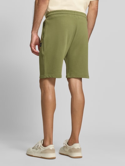 Männermodel trägt Shorts mit Label-Badge und elastischem Bund von Scotch & Soda in Olivgrün, Baumwolle, Regular Fit, Ganzkörperansicht Rückansicht.