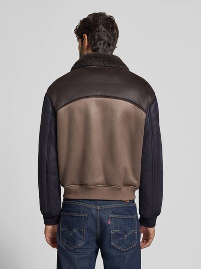Mężczyzna nosi Blouson in Leder-Optik mit Zweiwege-Reißverschluss von Armani Exchange, Materiał skóropodobny, krój regular fit, Wykładany kołnierz z futerka, zamek błyskawiczny dwustronny, widok całej sylwetki z tyłu.