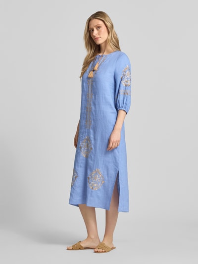 Frauenmodel trägt Tunikakleid aus Leinen mit Tunikakragen und Quasten von Emily Van den Bergh, midiblau, goldene Motiv-Stitchings, Loose Fit, lockere Textur, Ganzkörperansicht von vorne. Rückenlänge 118 cm, Brustweite 49 cm, Ärmellänge 42 cm.