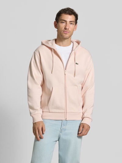 Männermodel trägt Regular Fit Sweatjacke aus Baumwoll-Mix von Lacoste in hellem Rosa, weiche Textur, Ganzkörperansicht von vorne.