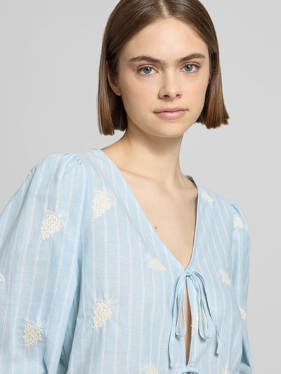 Frauenmodel trägt Bluse mit Schnürung Modell 'Ninon' von OH APRIL in Hellblau mit Weiß, Reine Baumwolle, Rüschenärmel, Nahaufnahme Oberkörper.