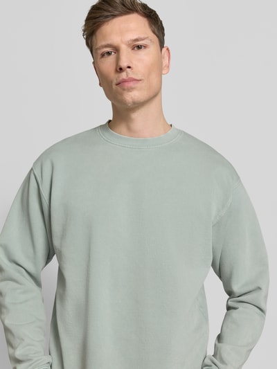 Mannenmodel draagt Sweatshirt aus reiner Baumwolle van Drykorn in lichtgroen, losse pasvorm, ribboorden, puur katoen, Nahaufnahme bovenlichaam.