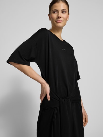 Modelka nosi T-Shirt-Kleid mit Rundhalsausschnitt und 1/2-Arm od ARMANI EXCHANGE, czarna bawełna, prosty krój, detal z logo, mini, półrękaw, Szerokość w rozmiarze S: 50 cm, długość tyłu: 82 cm, długość rękawa: 31 cm, zbliżenie na górną część ciała z przodu.