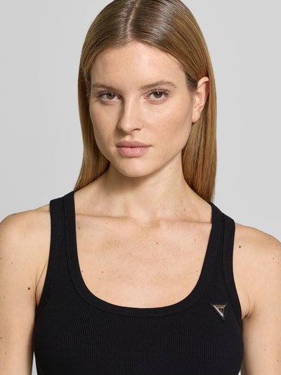 Frauenmodel trägt schwarzes, ärmelloses Slim Fit Top aus elastischem Viskose-Mix mit Logo-Applikation, Modell 'Colette' von Guess Activewear, Nahaufnahme Oberkörper.
