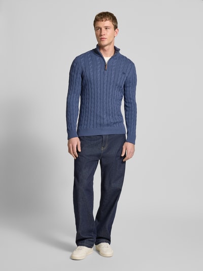 Männermodel trägt Strickpullover aus reiner Baumwolle von Superdry in Blau mit Zopfmuster, Troyer-Kragen, Label-Detail, gerippte Abschlüsse, enge Passform, Rückenlänge 70 cm, Ärmellänge 71 cm, Ganzkörperansicht von vorne.