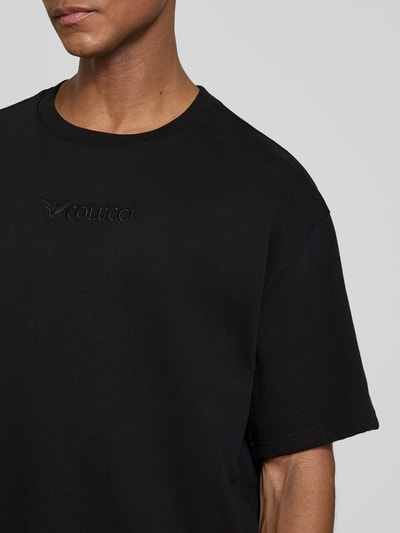 Männermodel trägt schwarzes Relaxed Fit T-Shirt mit Logo-Stitching Modell 'Ikarus' von COLUCCI, reine Baumwolle, Nahaufnahme Oberkörper.