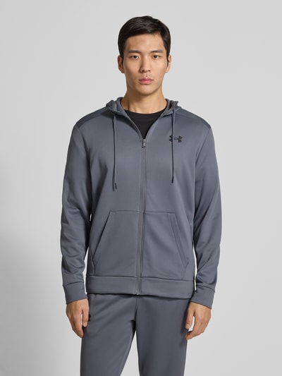 Männermodel trägt Sweatjacke mit Kapuze von Under Armour in Grau mit Lockerer-Schnitt, Tunnelzug, Reißverschluss, Label-Detail, Eingrifftaschen, gerippte-Abschlüsse, Rückenlänge 69 cm, Ärmellänge 66 cm, Ganzkörperansicht von vorne.