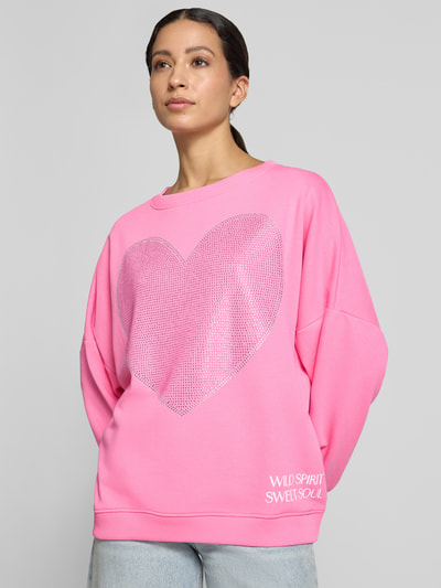 Vrouwenmodel draagt oversized sweatshirt uit puur katoen Model 'Sweet Soul' van miss goodlife in felroze met strass-steentjes en statementprint. Nahaufnahme Oberkörper.