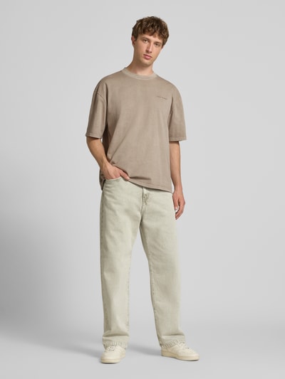 Männermodel trägt Oversized T-Shirt mit Label-Stitching von Pegador aus Baumwoll-Mix in Beige, Herren T-Shirt, Rundhalsausschnitt, Ganzkörperansicht von vorne, Rückenlänge bei Größe M 70 cm.