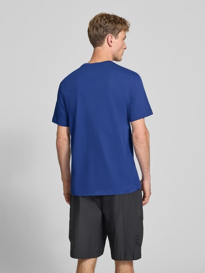 Männermodel trägt Regular Fit T-Shirt aus reiner Baumwolle von Nike in Blau zu schwarzen Shorts, Ganzkörperansicht Rückansicht.