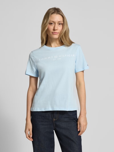 Frauenmodel trägt Regular Fit T-Shirt aus reiner Baumwolle von Tommy Hilfiger in Hellblau mit Logo-Schriftzug, Rundhalsausschnitt, kurzarm, Jersey, unifarben, Ganzkörperansicht von vorne.