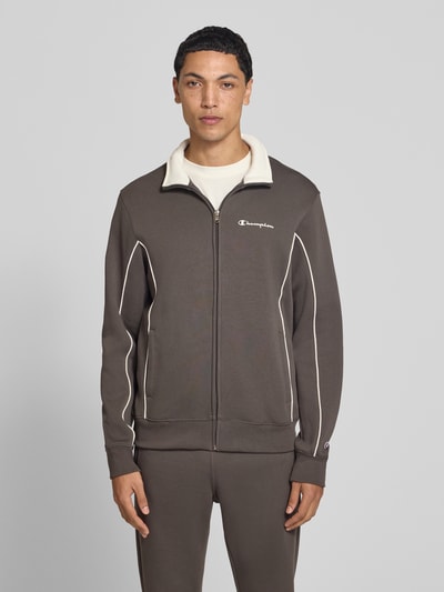 Männermodel trägt Trainingsanzug aus Baumwoll-Mix von Champion in Braun mit Kontrastnähten und Label-Prints, Ganzkörperansicht von vorne. Herren Trainingsanzug, gerade Passform, Stehkragen, durchgehender Reißverschluss, elastischer Bund und Abschlüsse, Größe M: Bundweite 42 cm, Rückenlänge 69 cm, Schulterbreite 50 cm, Ärmellänge 70 cm, Innenbeinlänge 78 cm.