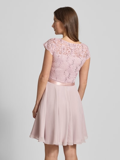 Młody modelka nosi Cocktailkleid mit Spitzenbesatz und Bindegürtel von SWING, róż o fakturze koronki i cekinach, A-linia, długość mini, widok całej sylwetki z tyłu.