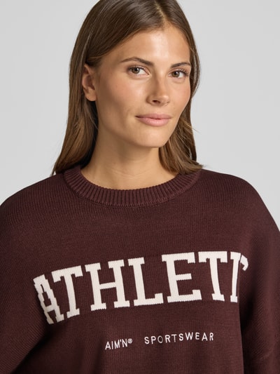 Frauenmodel trägt Oversized Strickpullover aus Viskose-Mix von aim'n in Dunkelrot mit Label-Stitching, Nahaufnahme Oberkörper.
