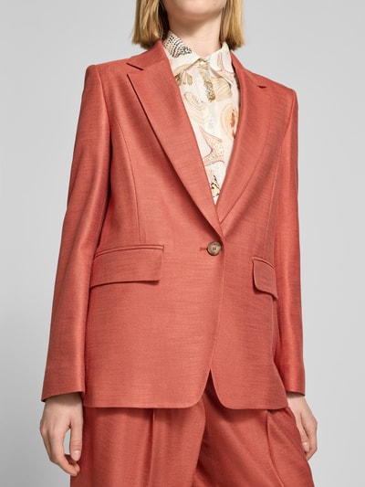 Frauenmodel trägt Slim Fit Blazer aus Viskose-Elasthan-Mix mit Pattentaschen von Marc Cain in warmem Rostrot, Knopfverschluss, Reverskragen, strukturierte glatte Textur, Ganzkörperansicht von vorne. Rückenlänge 68 cm, Brustweite 49 cm, Ärmellänge 62 cm, Größe 36.