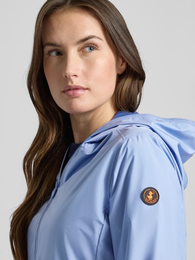 Modelka kobieca nosi Regular Fit Jacke mit Zweiwegereißverschluss Modell 'Stella' od SAVE THE DUCK w jasnoniebieskim kolorze, gładka faktura, z kapturem; damska kurtka z dwukierunkowym zamkiem, kieszeniami na zamek, długość tyłu w rozmiarze S: 60 cm, szerokość ramion w rozmiarze S: 42 cm, szerokość w rozmiarze S: 52 cm, długość rękawa w rozmiarze S: 64 cm; zbliżenie na górną część ciała z przodu.