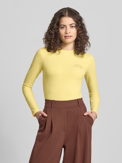 Frauenmodel trägt Slim Fit Longsleeve mit Logo-Detail von ANOTHER COTTON LAB in Gelb aus elastischem Baumwoll-Mix, Rundhalsausschnitt, Ganzkörperansicht von vorne.