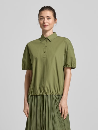 Frauenmodel trägt Regular Fit Bluse mit Polokragen von Marc Cain in Olivgrün, reine Baumwolle, elastische Ärmelabschlüsse, Bund mit Tunnelzug, kurzärmeliges Design, Ganzkörperansicht von vorne.