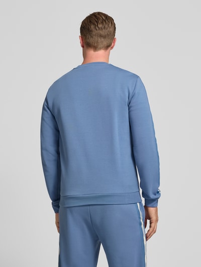 Männermodel trägt Sweatshirt mit Label-Patch und Rundhalsausschnitt von EA7 Emporio Armani in Blau, Baumwoll-Mix, Loose-Fit, Rückenansicht, Rückenlänge 67 cm, Ärmellänge 68 cm.