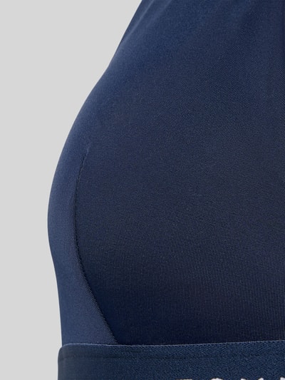 Vrouwenmodel draagt Badpak met Labelprint van Tommy Hilfiger in effen kleuren, gevoerd, voorgevormd, stretch. Detailopname bovenlijf.