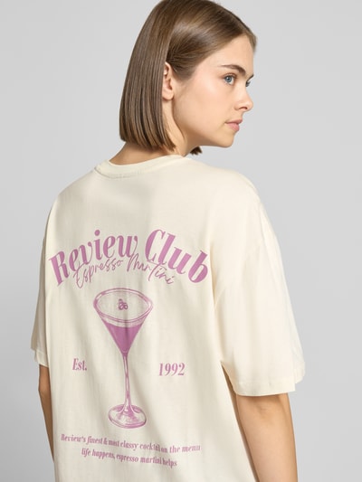 Frauenmodel trägt Oversized Fit T-Shirt aus reiner Baumwolle mit Label-Detail von REVIEW, cremefarben mit Print auf der Rückseite, Nahaufnahme Oberkörper.